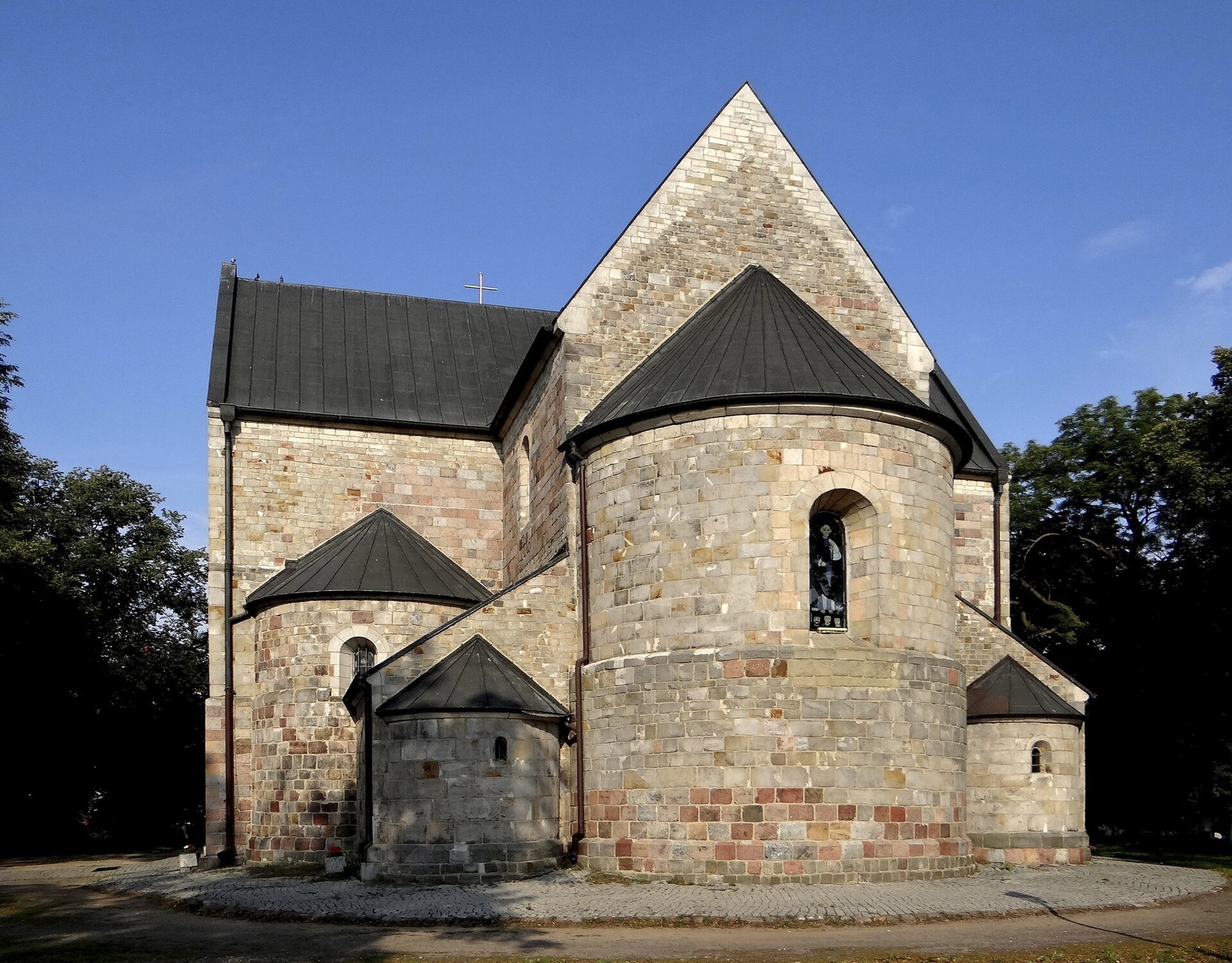 Zdjęcie przedstawia budynek bazyliki. Zbudowana jest z granitu i piaskowca. Ma ceglaną wieżę i półokrągłe apsydy.  