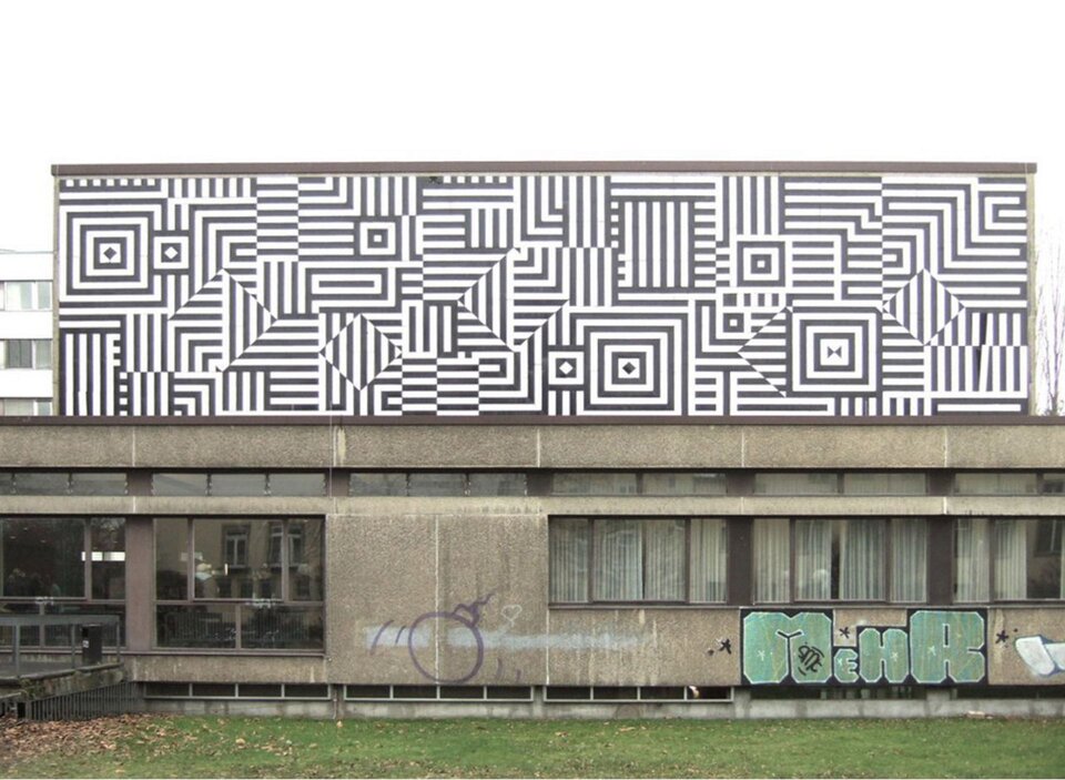 Ilustracja przedstawia dzieło Victora Vasarely „Ríu‑Kíu‑C”. Na ilustracji znajdują się wzory czarno‑białe. Składają się one głównie z kresek i tworzą różne kształty. Dzieło umieszczone jest na murze biblioteki Wydziału Prawa i Nauk Politycznych Uniwersytetu w Bonn. Poniżej widoczny jest fragment budynku oraz trawnika.