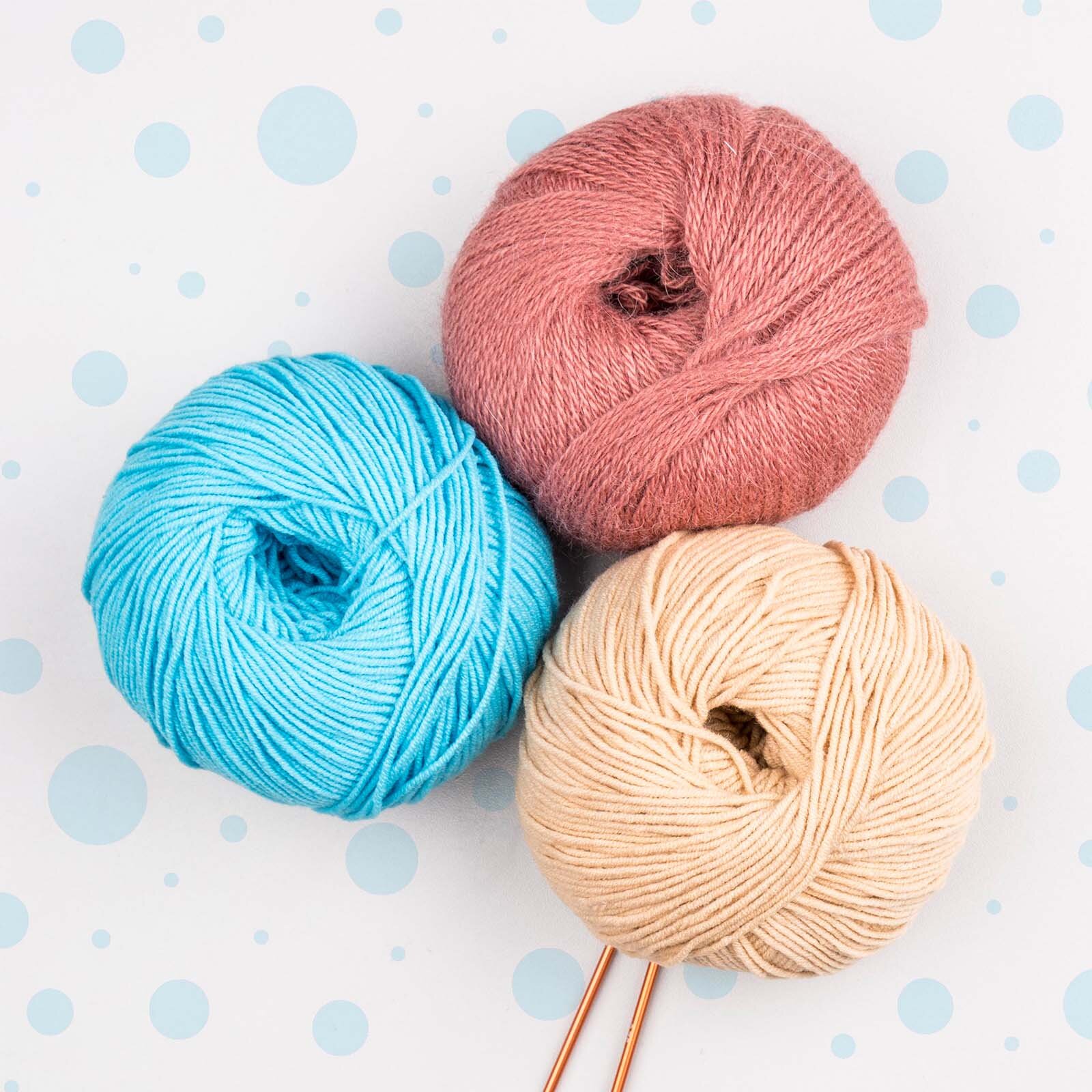 Zdjęcie przedstawia trzy motki wełny w kolorach niebieskim, różowym i żółtym.