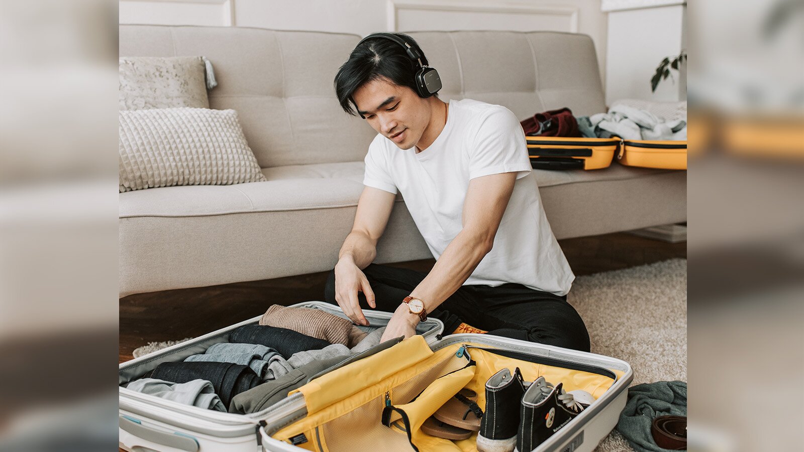 Zdjęcie przedstawia mężczyznę w młodym wieku pochylonego nad otwartą walizką. 