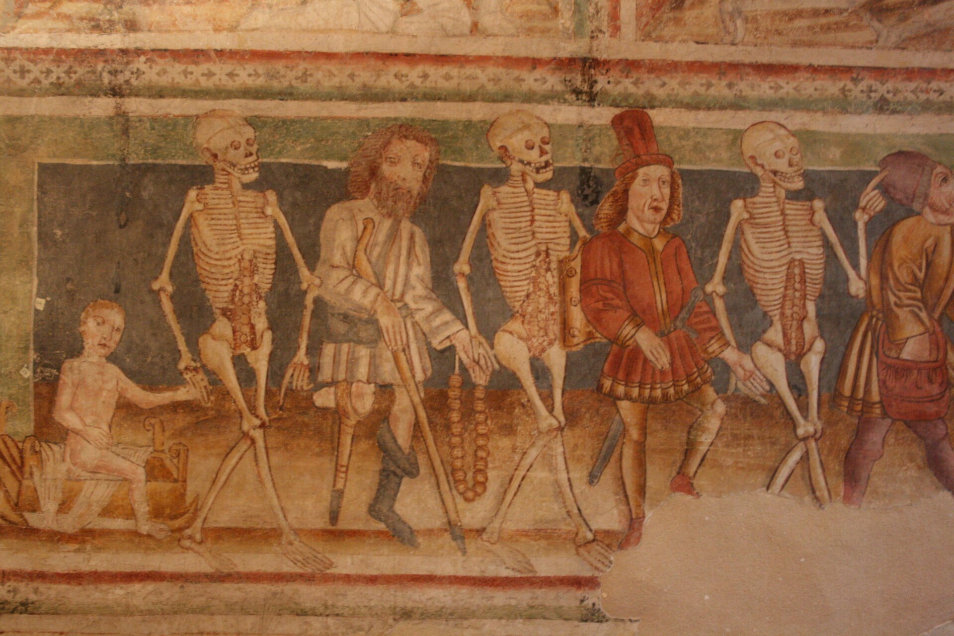 Ilustracja przedstawia grafikę: taniec szkieletów i ludzi. Korowód złożony jest naprzemiennie ze szkieletów i postaci ludzkich. Wszyscy trzymają się za ręce.