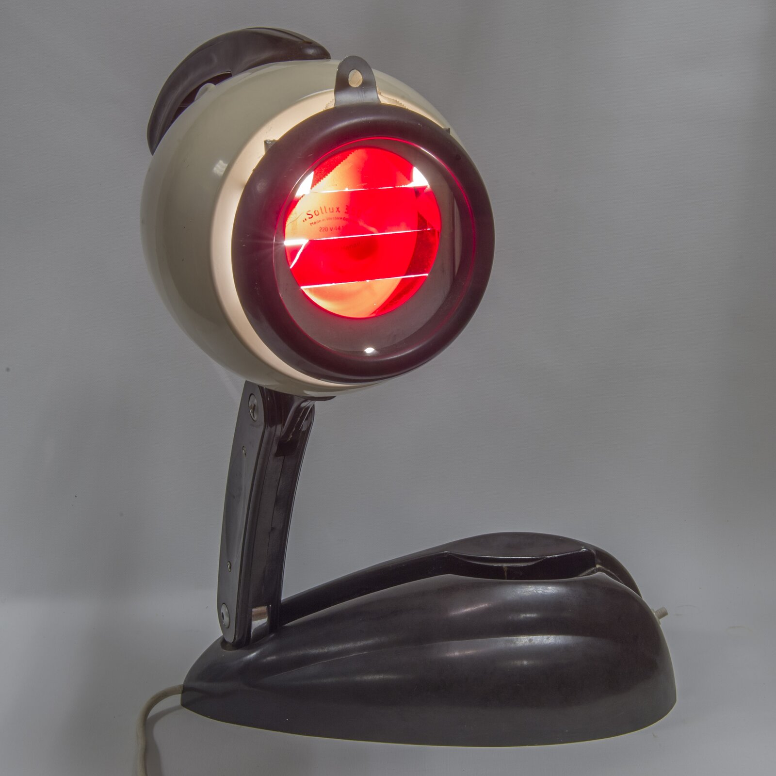 Rys. 2. przedstawia zdjęcie lampy na podczerwień na szarym tle. Lampa przypomina nowoczesną lampkę gabinetową w kolorze beżowo‑czarnym, lecz miejsce klasycznej żarówki zajmuje żarówka emitująca światło czerwone.