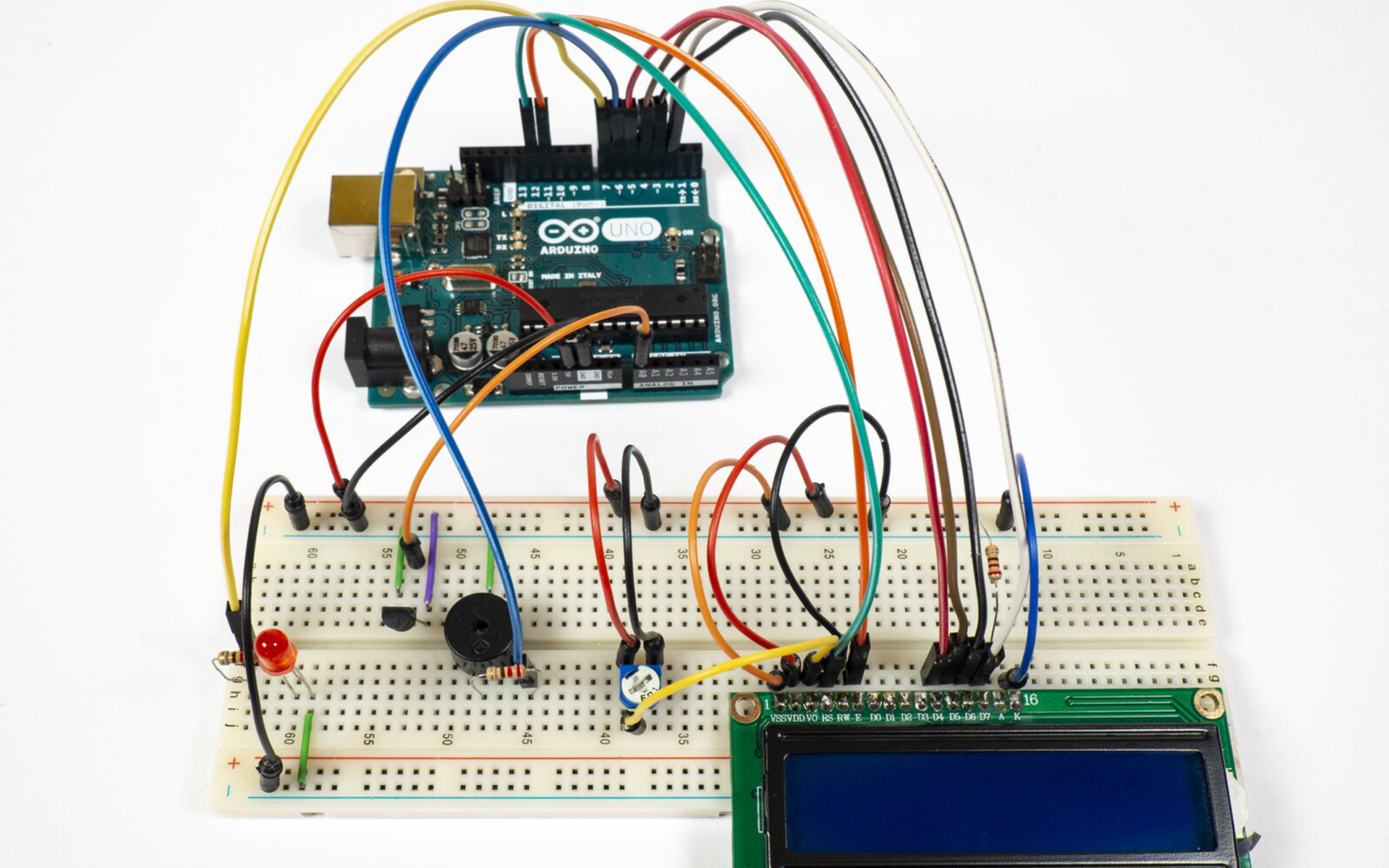 Zdjęcie przedstawia połączenia pomiędzy arduino uno, a płytką stykową. Na płytce znajduje się termometr (względem wycięcia w obudowie) podłączony jest prawą nóżką do uziemienia, lewą do +5V a środkową do pinu A0 arduino. Pin 5V podłączony jest do +5V płytki, a GND podłączone jest do uziemienia. Uziemienie górnej szyny jak i dolnej na płytce stykowej jest połączone. Podłączona jest także LED, jedną nóżką do uziemienia, drugą zaś poprzez rezystor do pinu 7 arduino. Po środku płytki zamontowany jest brzęczyk, który poprzez rezystor łączy się z pinem 6 arduino, a drugą nóżką do uziemienia. Po prawej stronie płytki stykowej podłączono ekran LCD, do którego podłączono kable prowadzące do arduino. Pomiędzy ekranem a brzęczykiem zamontowano potencjometr, do jego nóżek podłączono kable, środkowy do 3 pinu ekranu, lewa nóżka do +5V natomiast prawy do uziemienia. Ostatni i pierwszy pin ekranu podłączono do uziemienia płytki, przedostatni pin podłączono rezystorem do węzła dodatniego płytki. Do 2 pinu ekranu dołączono kabel z węzła dodatniego płytki. Pin 5 ekranu podłączono do szyny dodatniej.