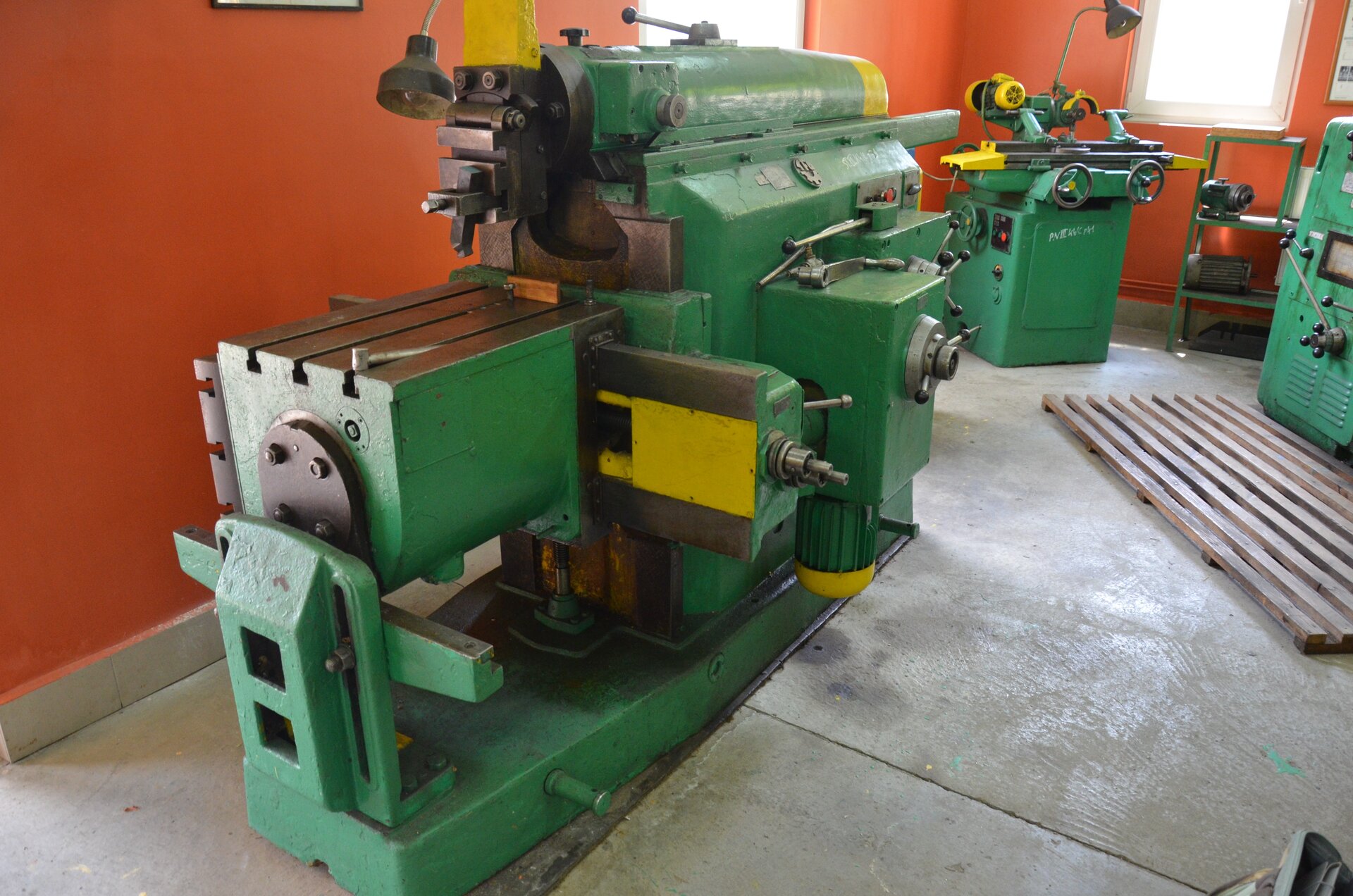 Strugarka przedstawiona na ekranie składa się z blatu, na którym ustawia się materiał do strugania, rolki dociskowe, które utrzymują materiał na miejscu, a także z dwóch cylindrów tnących z nożami.