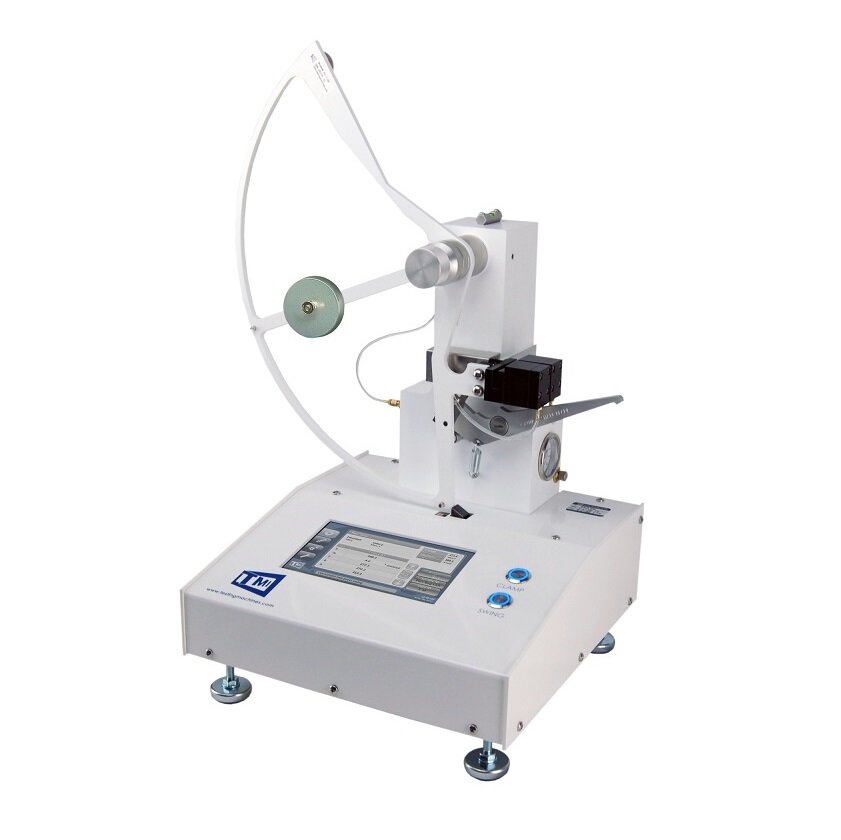 Zdjęcie ukazujące Aparat Elmendorfa. Prostokątna, płaska podstawa aparatu stoi na czterech metalowych nóżkach o regulowanej wysokości. Z przodu podstawy znajduje się dotykowy monitor to programowania maszyny, oraz dwa okrągłe przyciski. Z tyłu podstawy maszyny znajduje się ramię, do którego po lewej stronie przymocowano ruchome półkole z okrągłym odważnikiem.