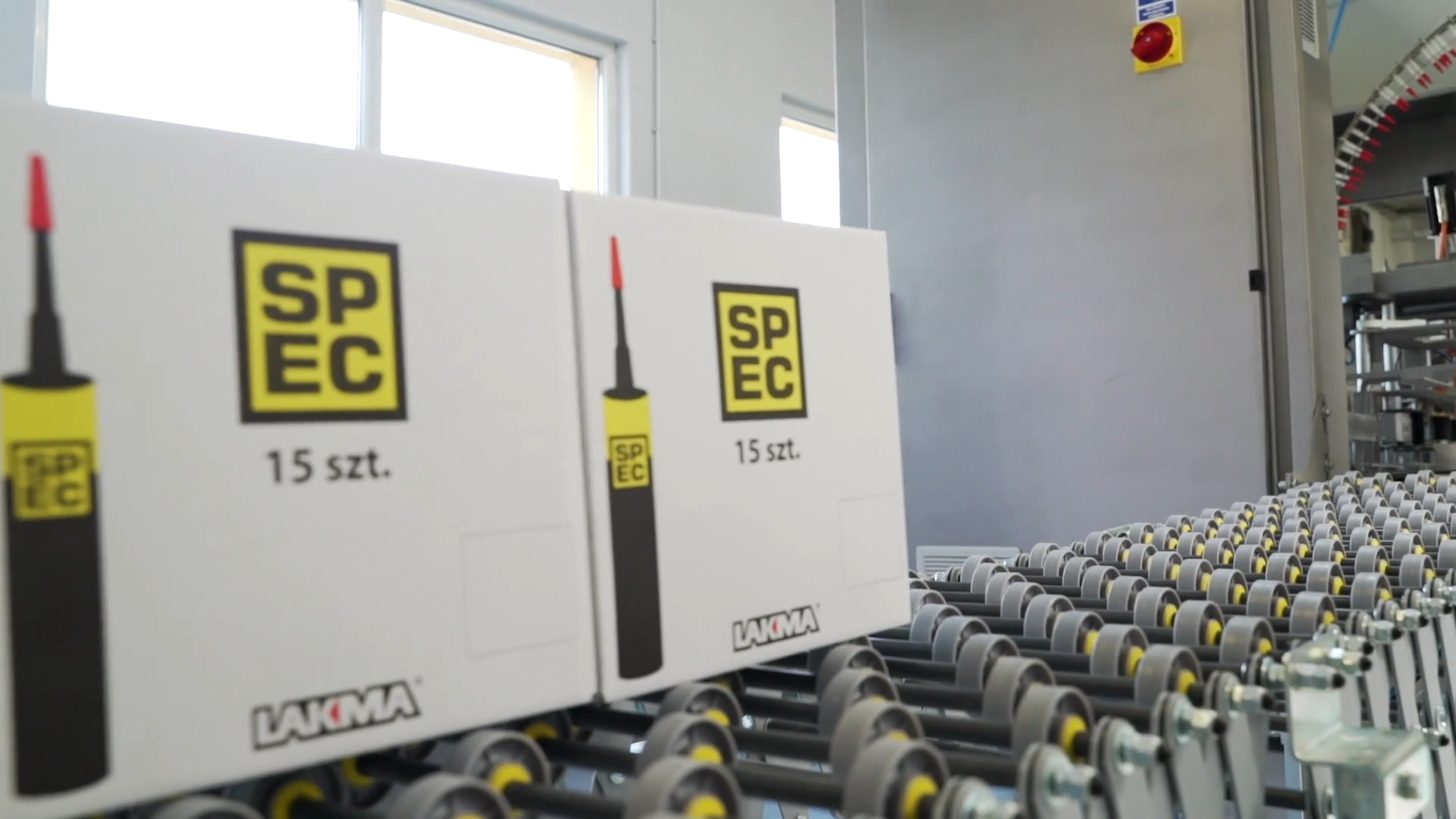 Zdjęcie przedstawia dwa opakowania zbiorcze. Są to kartonowe pudełka przesuwające się po przenośniku rolkowym.