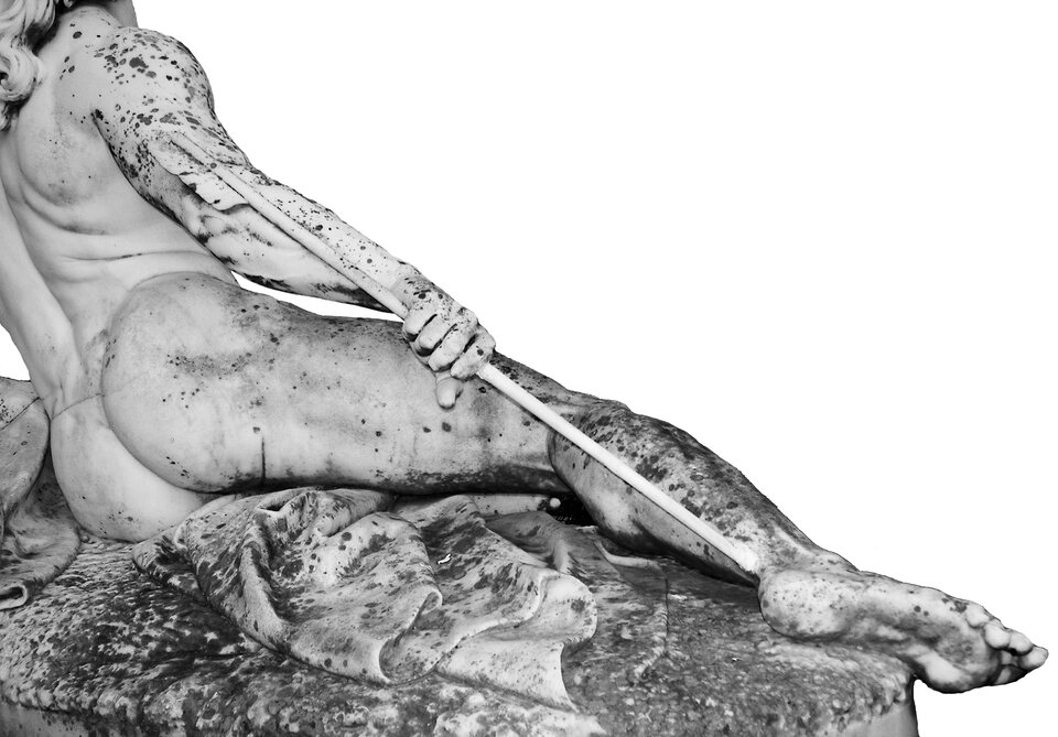 Kliknij, aby powiększyć Poziomo zorientowany fragment rzeźby „Umierający Achilles”. Widoczny fragment rzeźby wypełnia całkowicie część kadru poniżej jego przekątnej wytyczonej z dolnego prawego narożnika do lewego górnego. Półleżąca na cokole, pięknie umięśniona, idealizowana postać herosa, została sfotografowana od tyłu, z tym że głowa skrywa się poza kadrem u zbiegu jego krawędzi w górnym narożniku. Kadr nie obejmuje także przyciętej pionową linią krawędzi lewej łopatki, barku i ręki, na której wspiera się uniesiony niemal do pionu, podany ku prawej stronie tors. Prawa noga nieznacznie ugięta w kolanie spoczywa na ukazanej realistycznie na szczycie cokołu ziemi wyścielonej płaszczem wojownika, a koniec jego stopy, zamykając kompozycję w lewym narożniku kadru, wystaje częściowo poza cokół. Ranny zacisnął prawą dłoń w połowie długości strzały, która utkwiła w jego pięcie, sięgając z drugiego końca pierzastym bełtem powyżej biodra. Poziome płaszczyzny jasnego kamienia pokrywają ciemne plamy porostów.