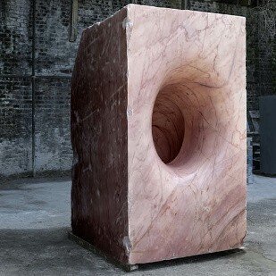 Zdjęcie przedstawia wydrążony blok marmuru w galerii sztuki. Okrągły ażur został gładko oszlifowany. Rzeźba została wykonana przez światowej sławy artystę Anisha Kapoora.