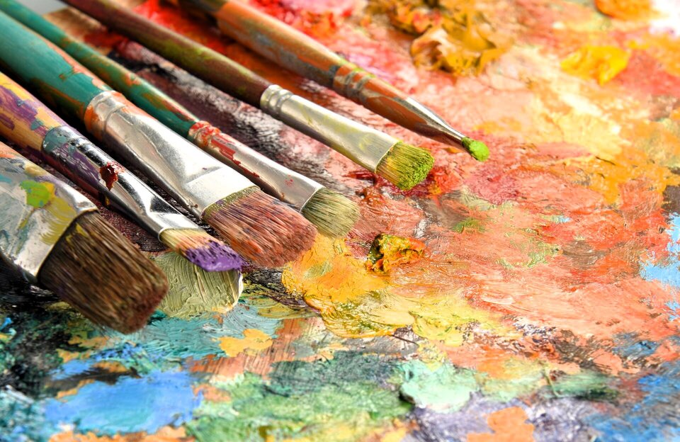 Obraz przedstawia kilka pędzli ubrudzonych farbą na płaskiej powierzchni palety, pokrytej farbą olejną.