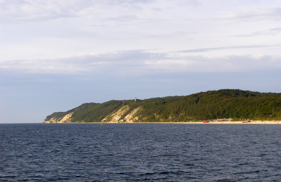 Fotografia przedstawia morze i nadmorskie łagodne grzbiety, porośnięte lasem. To klif w Wolińskim Parku Narodowym.