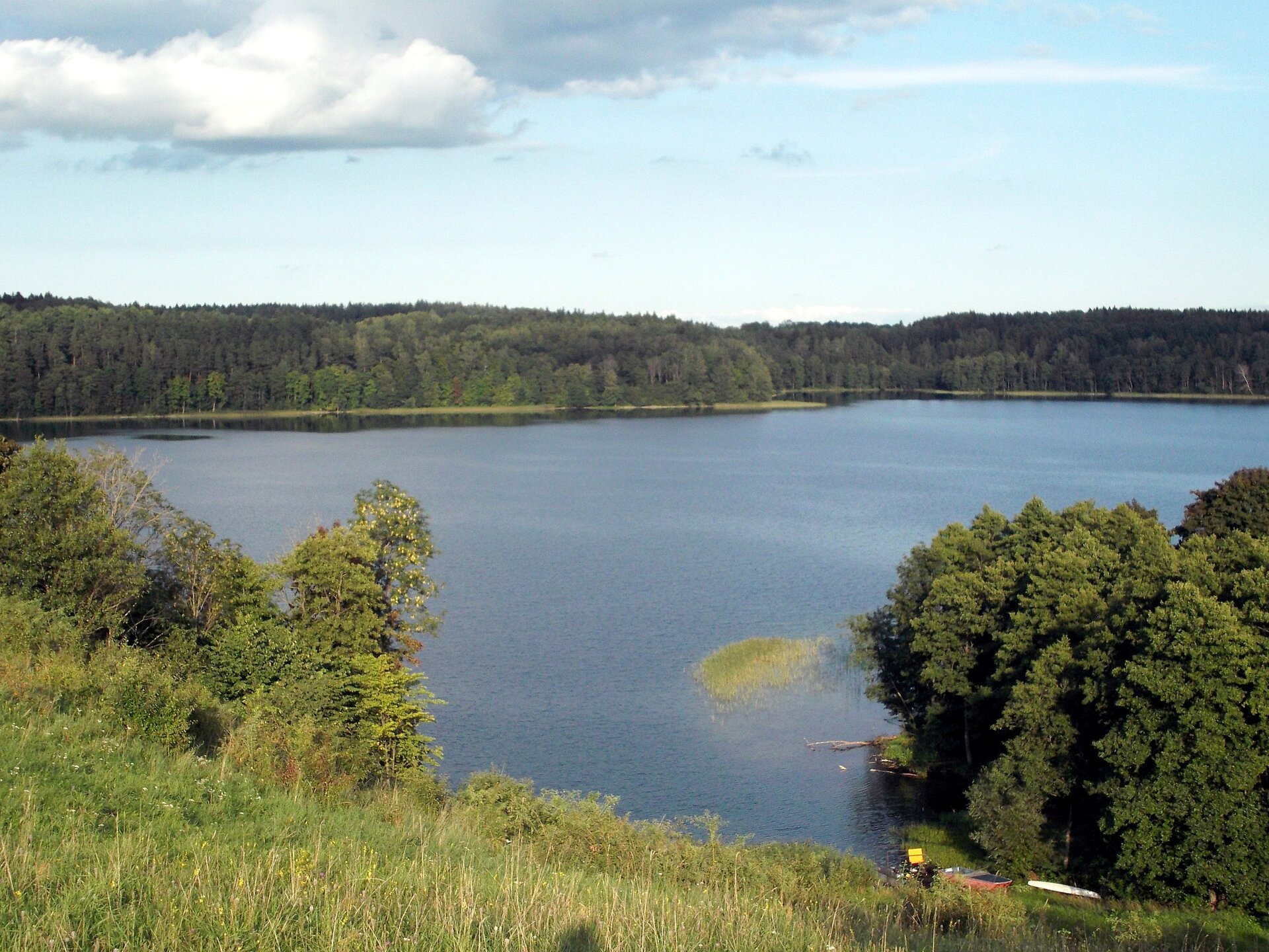 Zdjęcie niewielkiego jeziora otoczonego lasami mieszanymi.