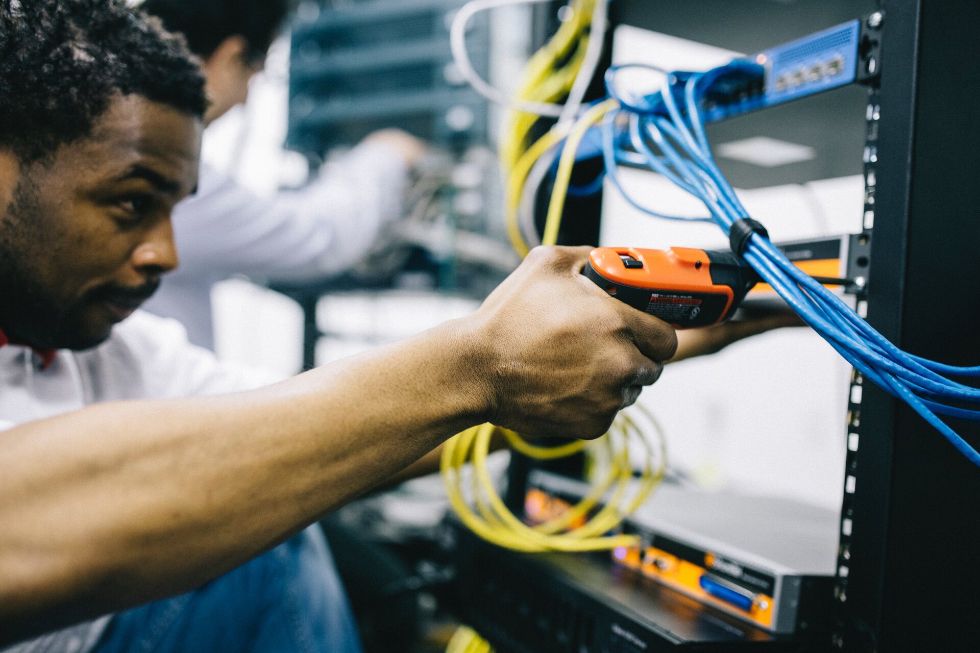 Zdjęcie przedstawia montera, który za pomocą wkrętaka elektrycznego montuje urządzenie elektryczne w metalowej obudowie.