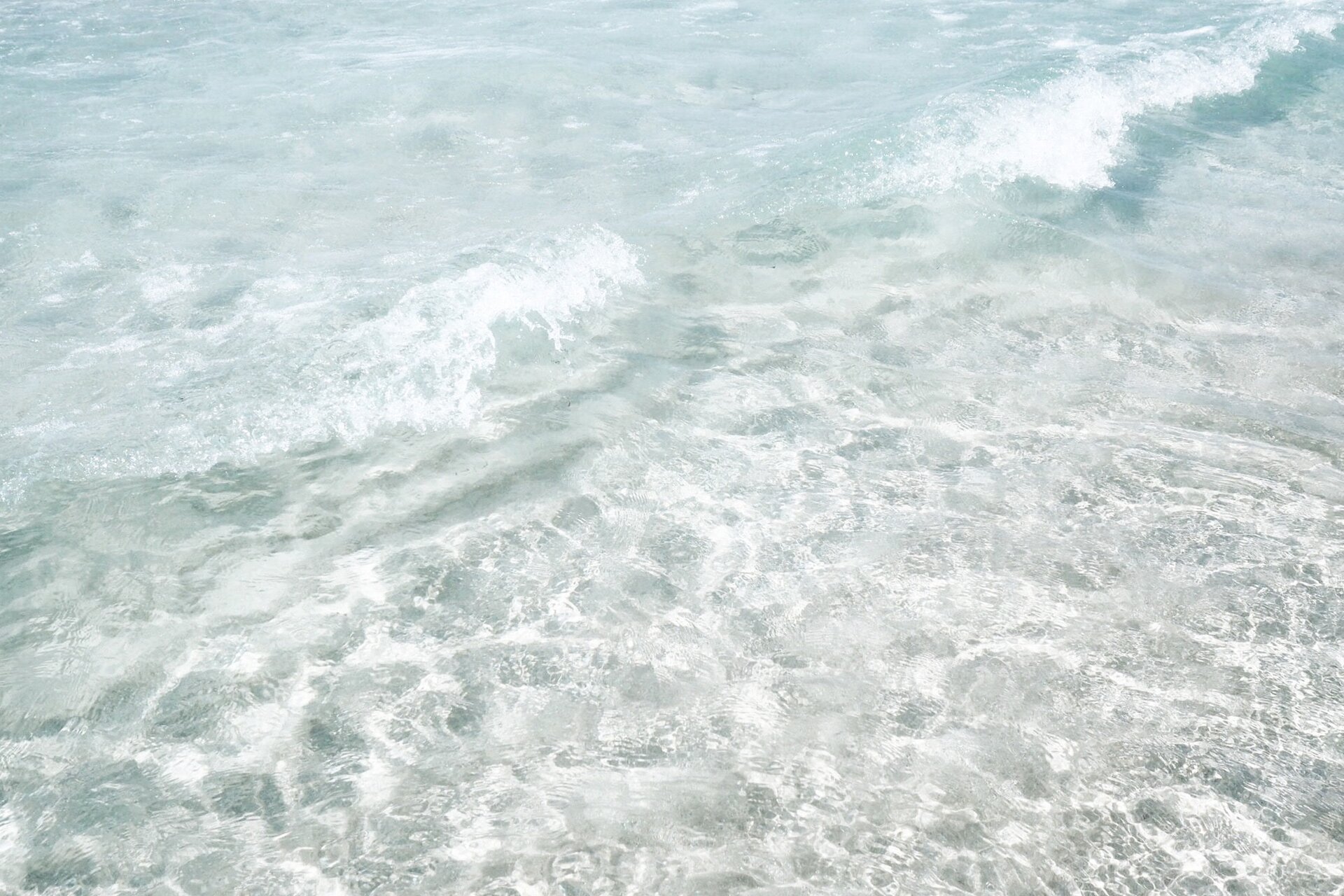 Zdjęcie przedstawia delikatną falę napływającą z lewej strony oraz krystalicznie czystą wodę zbiornika wodnego. 