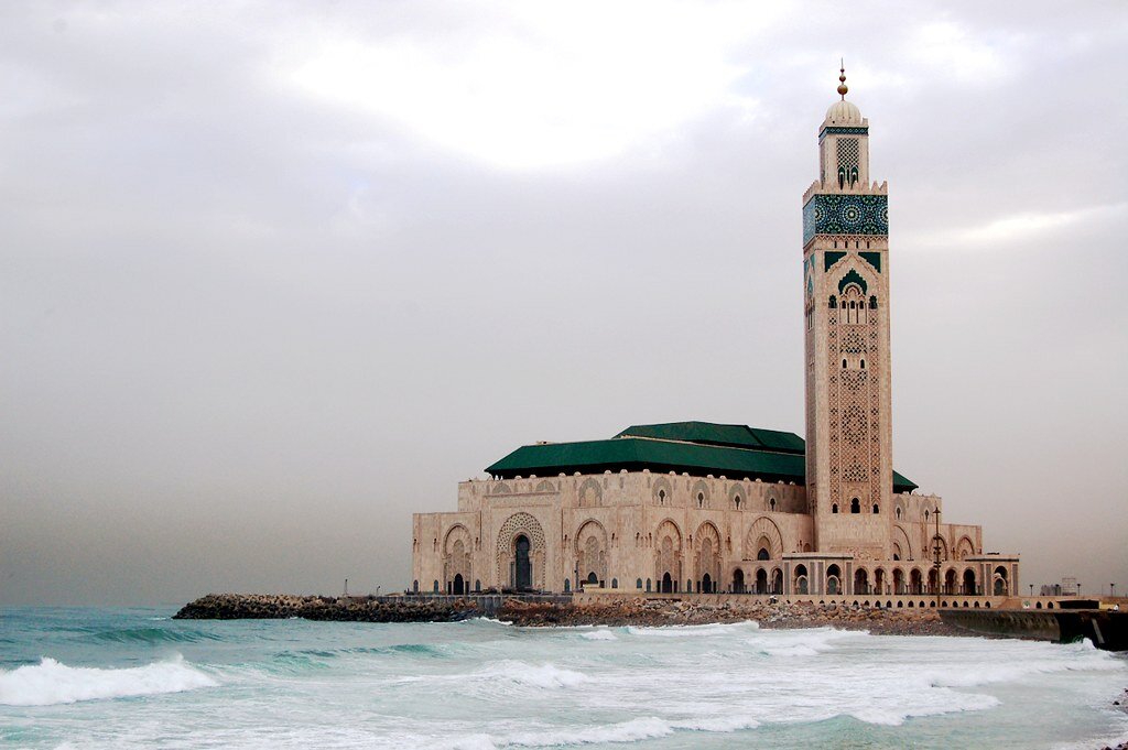 Na zdjęciu znajduje się Meczet Hasana drugiego. Jest to jasna przysadzista budowla o zielonym dachu. Po jej prawej stronie widoczny jest wysoki minaret. Jej ściany są pokryte licznymi łukami i zdobieniami. Świątynia jest umiejscowiona na wybrzeżu morza. 