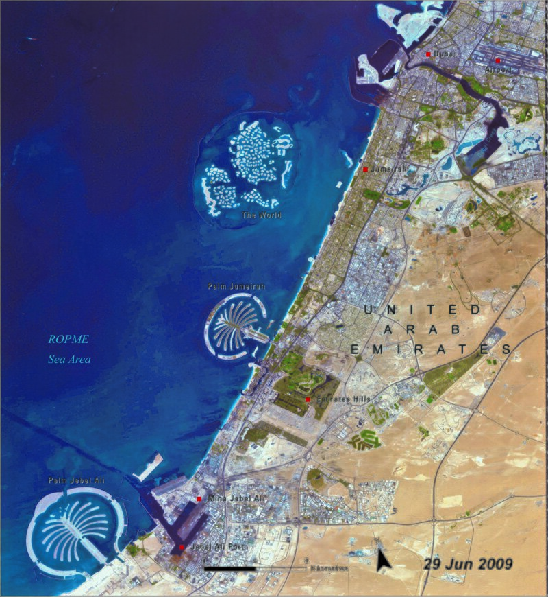 Na fotografii z 2009 roku widać wybrzeże Zjednoczonych Emiratów Arabskich we fragmencie, w którym znajduje się Dubaj. Pokryte jest w całości licznymi budynkami, drogami, a także sporymi zielonymi plamami. Są to sztucznie stworzone tereny zielone.  W ląd w górze obrazka wrzyna się zatoka, na dole widać zarys portu. Zatoka Perska ma kolor niebieski, na jej tle widać sztuczne wyspy stworzone przez człowieka – dwie w kształcie palmy i jedna imitująca układ kontynentów na mapie świata. 