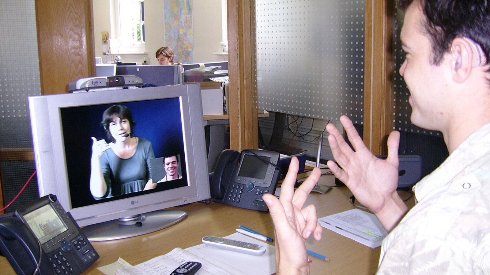 Zdjęcie przedstawia osobę siedzącą przy biurku, która prowadzi rozmowę z osobą widoczną na komunikatorze w komputerze. 