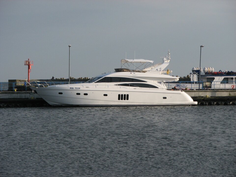Zdjęcie przedstawia dużą, białą, luksusową łódź motorową. Stoi w porcie. 