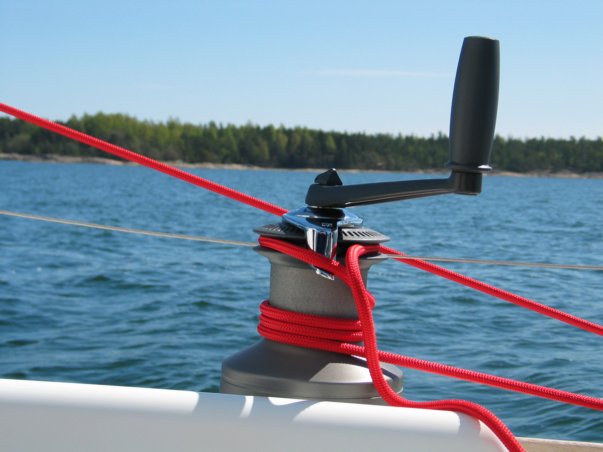 Ilustracja przedstawia kabestan zamontowany na łodzi. Jest to urządzenie z okrągłą korbową rączką, wokół którego widoczne są napięte liny. 