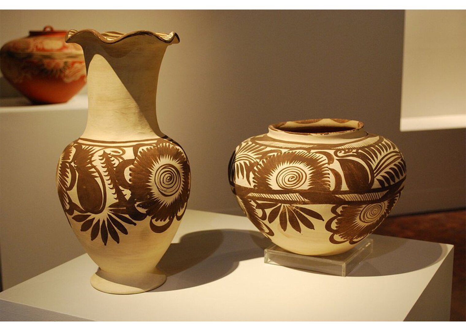 Na zdjęciu dwa jasnobrązowe wazony  - różnej wielkości - wykonane z gliny. Na wazonach ciemnobrązowe zdobienia - kwiaty.