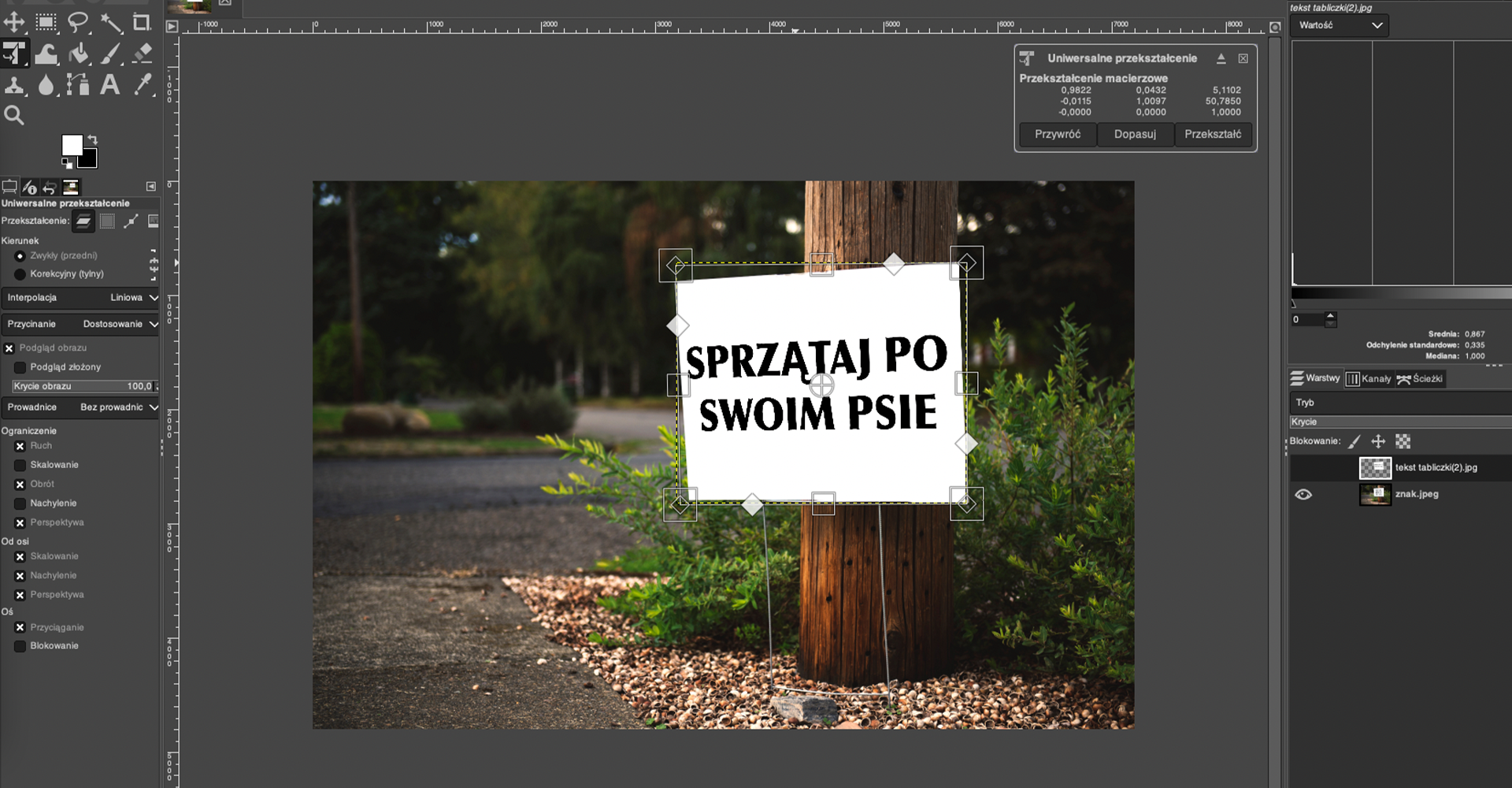 Ilustracja przedstawia okno programu. Panel po lewej stronie dotyczy przekształcenia. W obszarze roboczym jest zdjęcie przedstawiające białą tablicę stojącą na skwerze. Na tablicy napis: SPRZĄTAJ PO SWOIM PSIE. Tablica stoi przy drewnianym pniu. W tle są niskie zielone krzewy i drzewa. Nad zdjęciem po prawej stronie jest panel dotyczący Uniwersalnego przekształcenia, tam przekształcenie macierzowe z parametrami. Po prawej stronie jest panel dotyczący wartości oraz warstw. Wybrano warstwę o nazwie: tekst tabliczki(2).jpeg.  