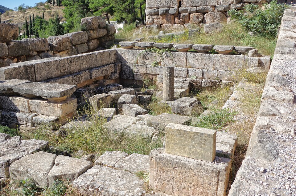 Fotografia przedstawia ruiny skarbca Syfnijskiego z Delf - są tu ruiny budowli, z widoczną roślinnością wśród ruin.