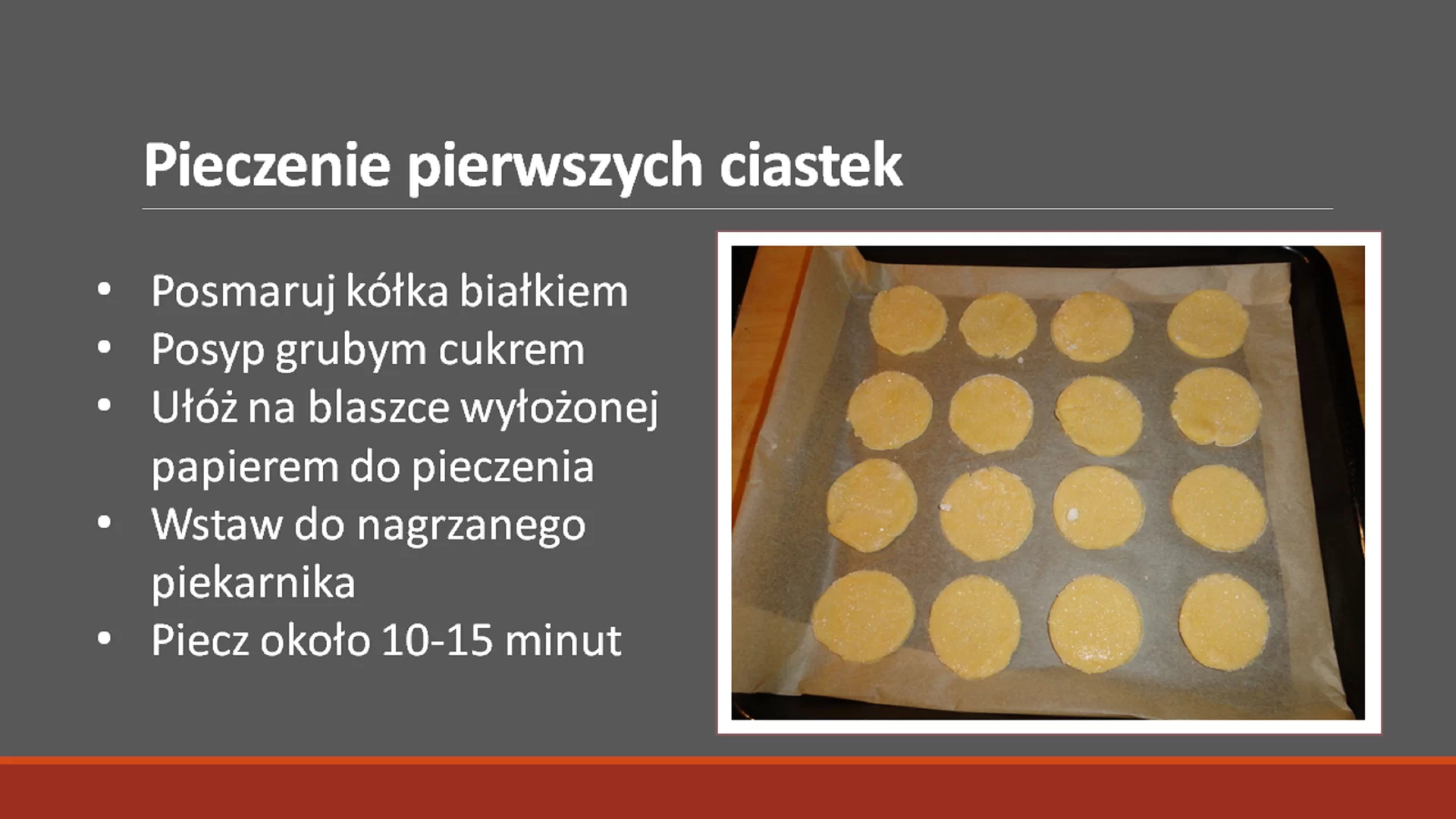 Czwarty slajd pod tytułem: "Pieczenie pierwszych ciasteczek". Tytuł ma pogrubioną i większą czcionkę. Pod nim znajduje się tekst: "Posmaruj kółka białkiem. Posyp grubym cukrem. Ułóż na blaszce wyłożonej papierem do pieczenia. Wstaw do nagrzanego piekarnika. Piecz około 10‑15 minut.". Tekst jest napisany w punktach. Obok niego, po prawej stronie znajduje się zdjęcie w ramce przedstawiające ciasteczka rozłożone na blaszce wyłożonej papierem do pieczenia.