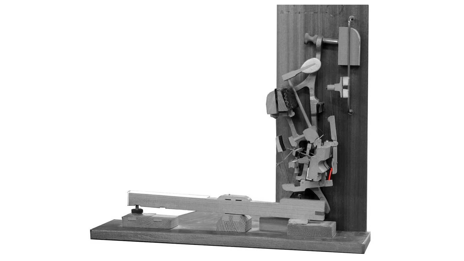 Zdjęcie przedstawia podzespół mechanizmu pianinowego lub fortepianowego jakim jest łyżeczka dźwigni głównej. Element został zaznaczony czerwoną obwódką, a dodatkowo pozostałe elementy są w odcieniach szarości dla lepszego uwidocznienia.