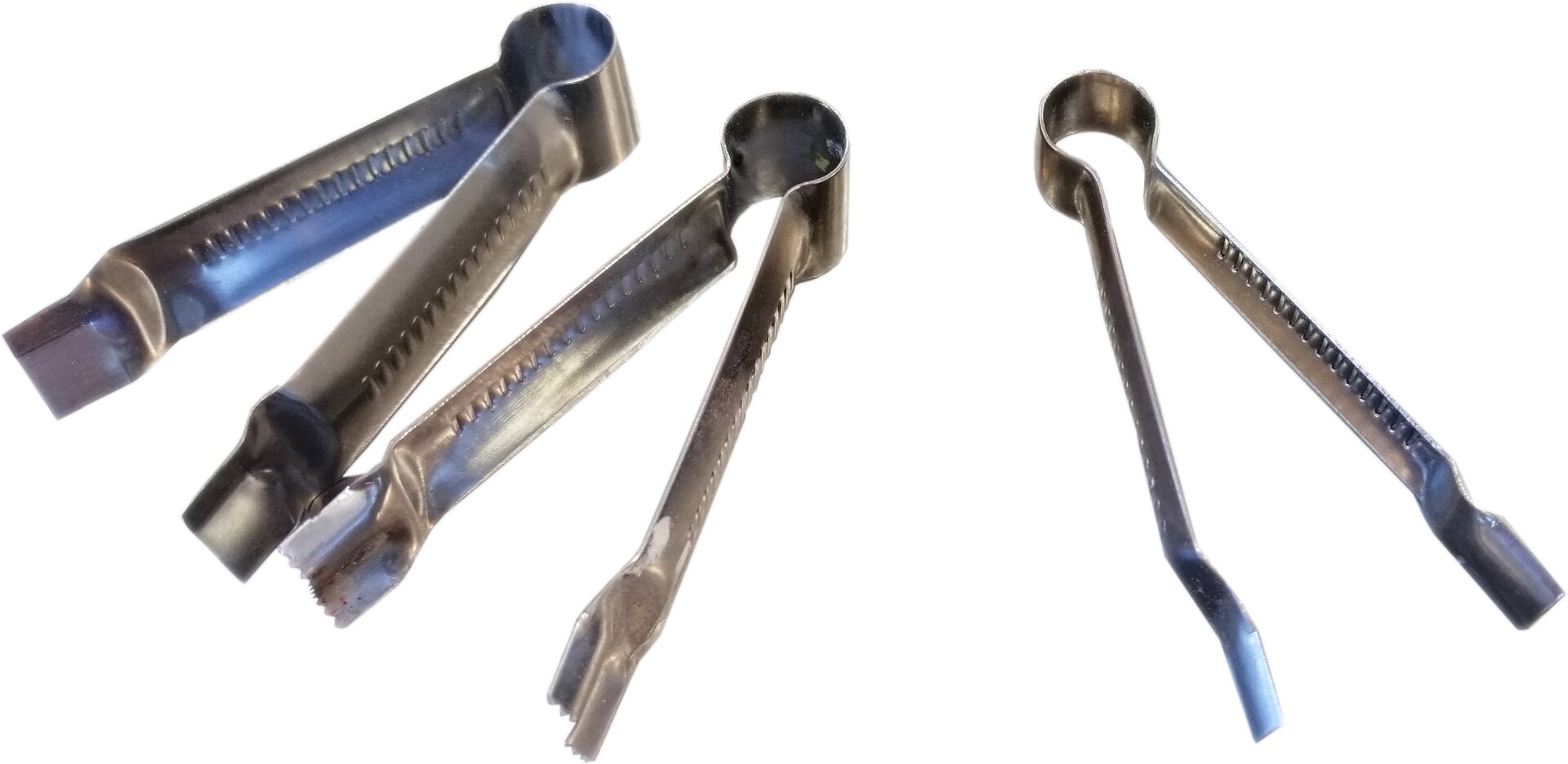 Zdjęcie przedstawia szczypce dekoratorskie. Widoczne są trzy sztuki metalowych szczypiec. Widoczne są dwa ramiona, które w górnej części są ze sobą połączone w taki sposób, aby sprężynowały, jednocześnie tworzące półokrągły uchwyt. Ramiona zakończone są łopatkowatymi, płaskimi końcówkami roboczymi.