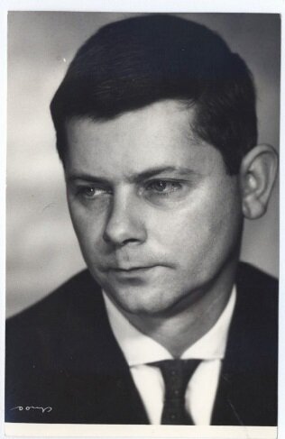 Czarno‑białe zdjęcie, które przestawia Zbigniewa Herberta. Ma on krótkie włosy, które są zaczesane na bok. Jest ubrany w białą koszulę i ciemną marynarkę. 