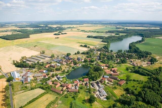 Ilustracja przedstawia wieś w województwie lubuskim. Jest ona skupiona dookoła zbiornika wodnego.