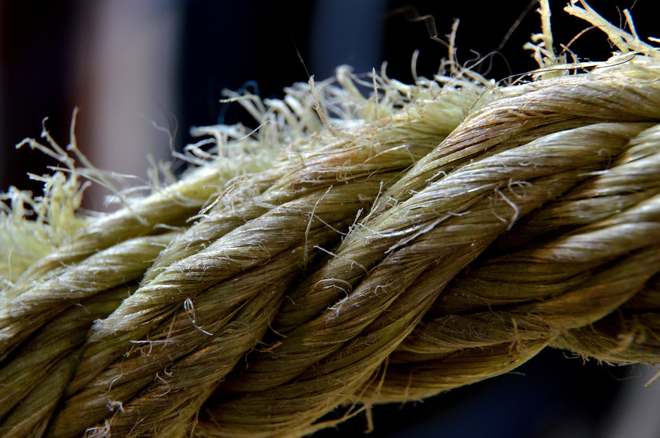 Ilustracja przedstawia zbliżenie grubego, skręconego sznura wykonanego z naturalnych włókien roślinnych. Włókna są wyraźnie widoczne – niektóre wystają z powierzchni, mają chropowatość i strukturę. Sznur jest skręcony z kilku cieńszych pasm, tworząc wytrzymałą, spiralną formę. Tło jest rozmyte. 