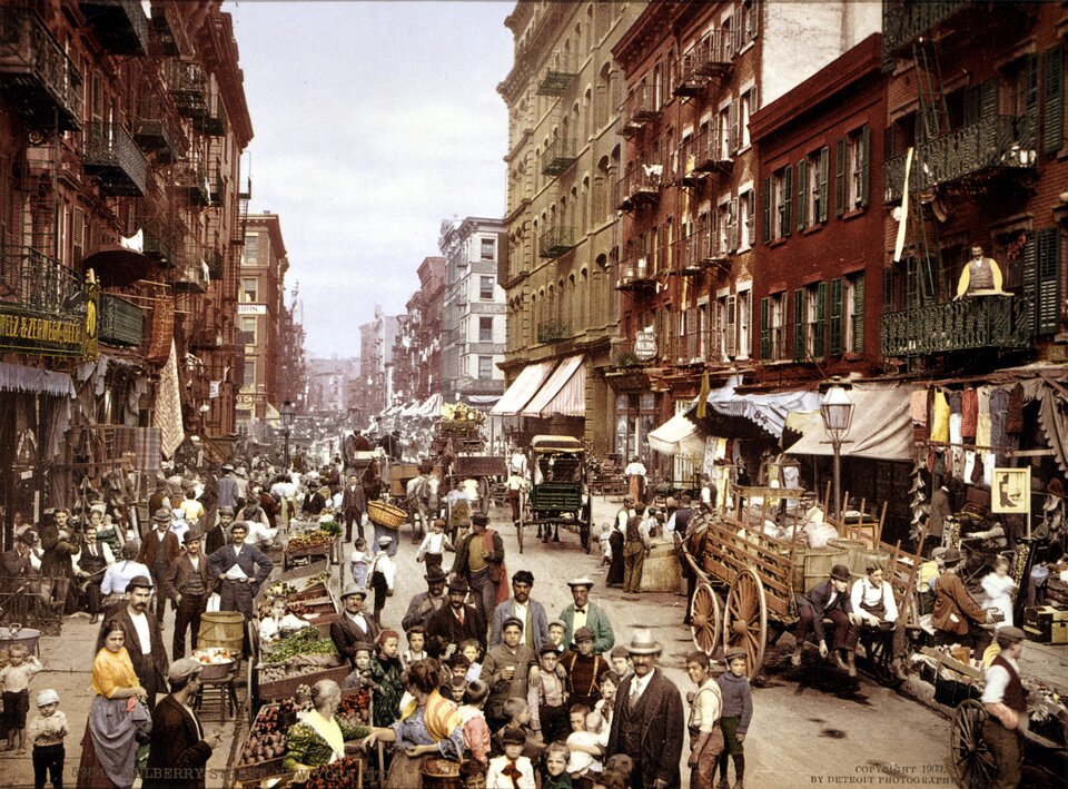 Lower East Side – dzielnica, w której mieszkała rodzina Gershwina. Na ilustracji widzimy po lewej i prawej stronie stare kamienice. Na ulicy znajdują się kupcy i sprzedawcy oraz wozy z koniem.