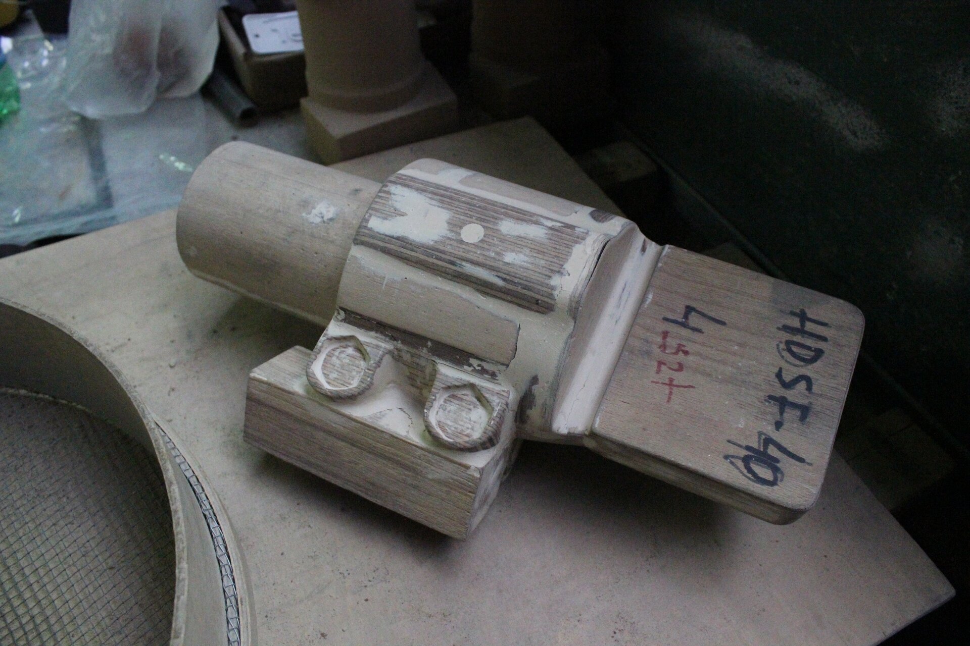 Ilustracja przedstawia model drewniany z jasnymi elementami na powierzchni, które stanowią wypełnienie ubytków modelu. Model ma skomplikowany kształt i leży na stole roboczym.