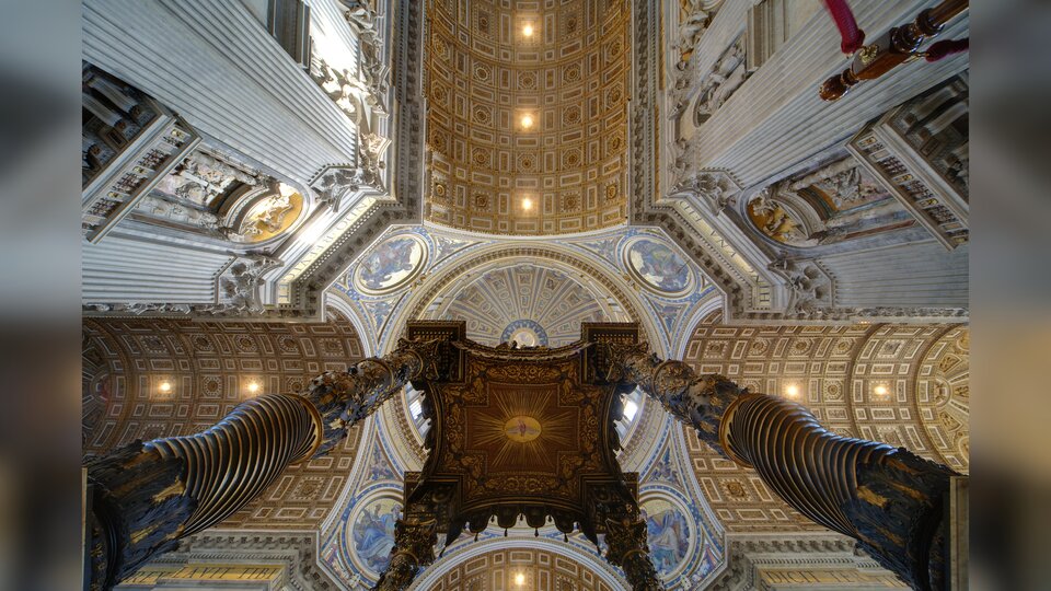 Zdjęcie przedstawia sufit bazyliki. Jest on zbudowany w kształcie krzyża, z wieloma zdobieniami i misternymi malowidłami.