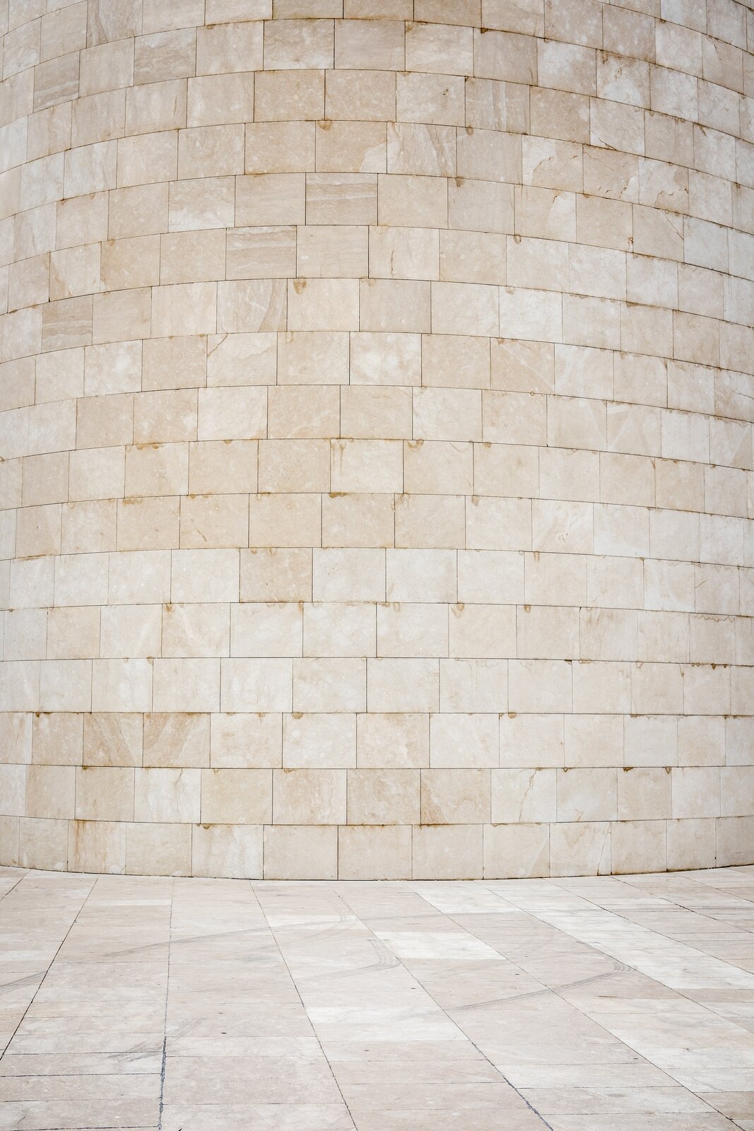 Zdjęcie przedstawia szlifowaną powierzchnię ściany ustawionej na zewnątrz, która składa się z jasnopomarańczowych kamieni o regularnym kształcie i gładkiej, równej fakturze.