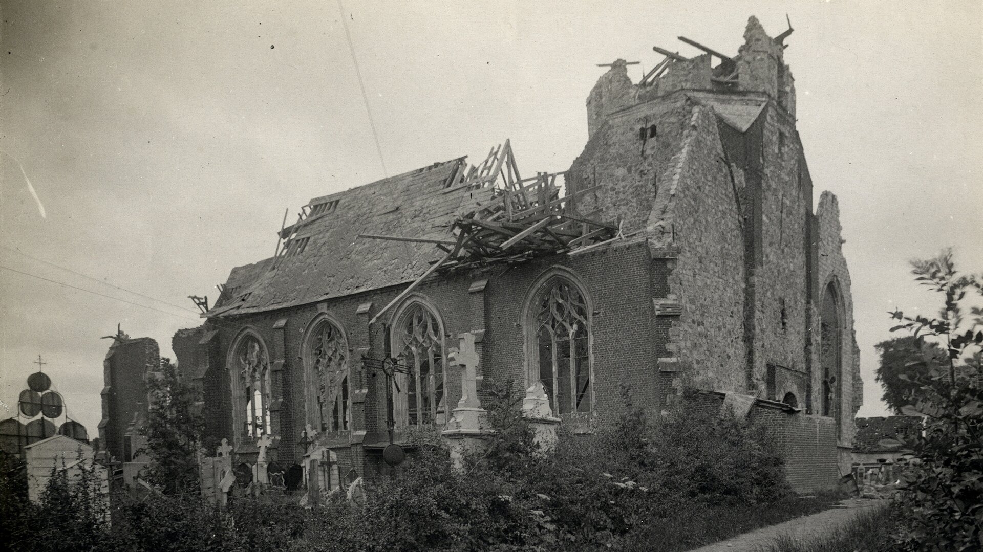 Fotografia czarno-biała przedstawiająca kościół w Richebourgu zniszczony przez ostrzał niemiecki. Widać zawalony, zniszczony całkiem dach, walące się ściany. Na pierwszym planie zniszczony przykościelny cmentarz.