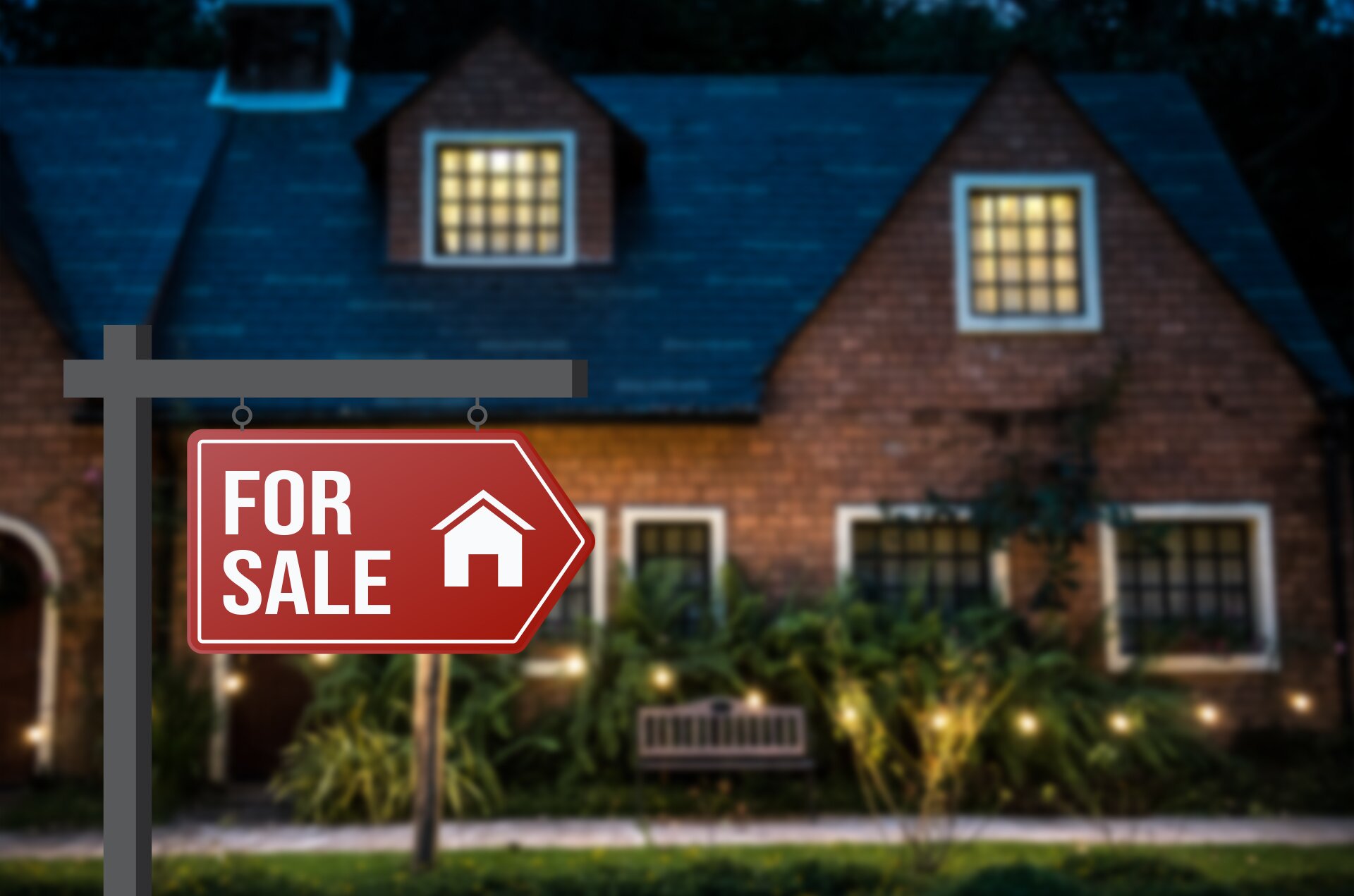 Zdjęcie przedstawia dom jednorodzinny wykonany z cegły ze spadzistym dachem. Przed domem znajdują się krzewy. Na pierwszym planie jest czerwona tabliczka z wizerunkiem domku i napisem For sale.