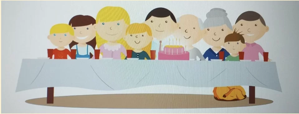 Przy dużym stole siedzi dziewięcioosobowa rodzina, każda z osób jest uśmiechnięta. Na stole jest tort, talerzyki i kubki. Pod stołem śpi piesek.
