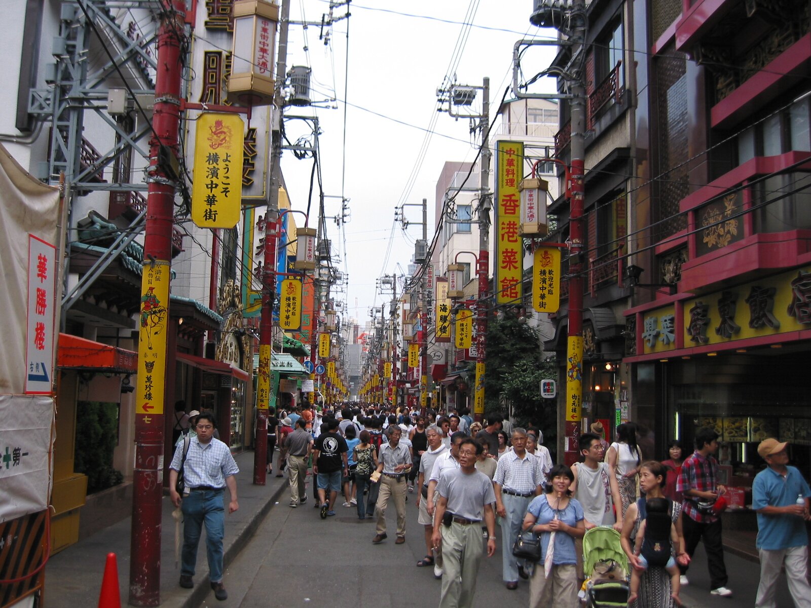 Zdjęcie przedstawia ulicę w mieście, na której jest dużo ludzi. Ulica znajduje się pomiędzy wysokimi budynkami. Na budynkach są liczne szyldy w języku chińskim.  
