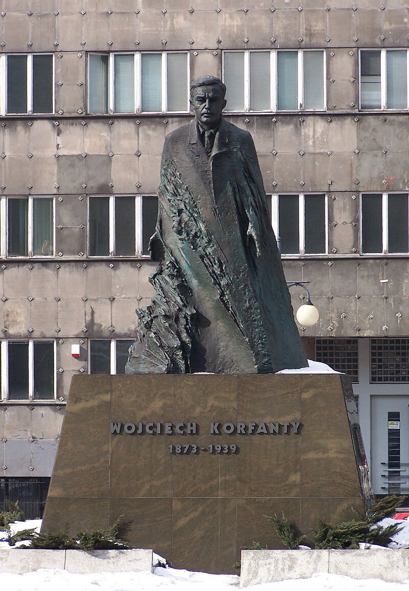 Na zdjęciu widoczny jest pomnik mężczyzny. Ubrany jest w płaszcz, koszulę i krawat. Na pomniku widnieje napis: Wojciech Korfanty 1873‑1939.