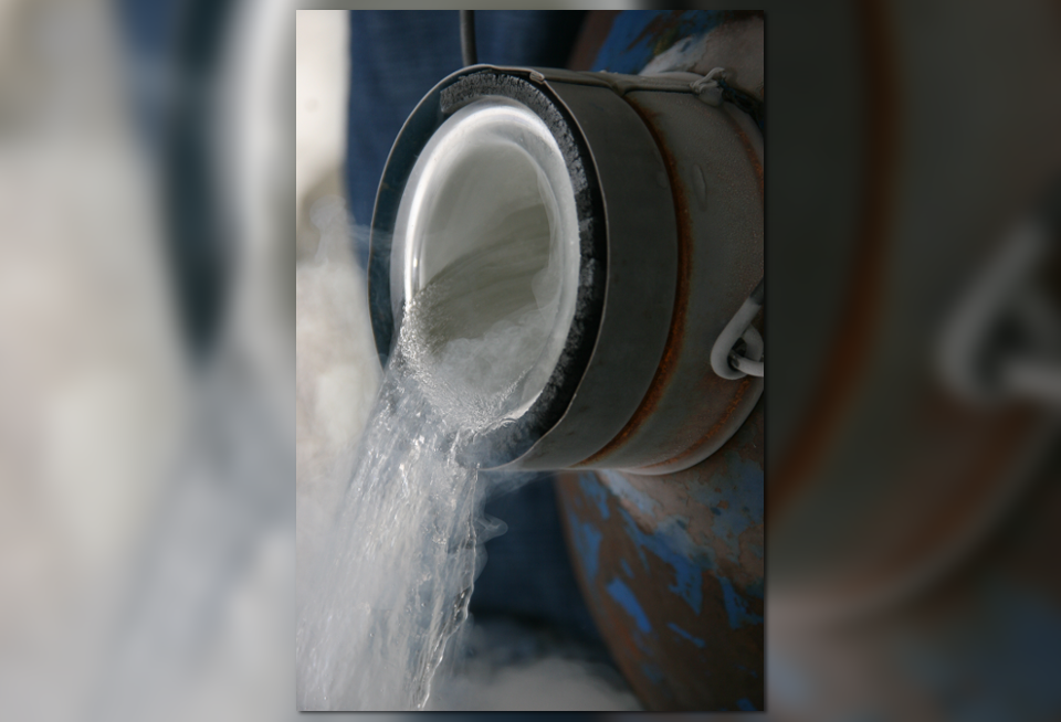 Fotografia przedstawia ciekły azot wypływający z przewróconej beczki.