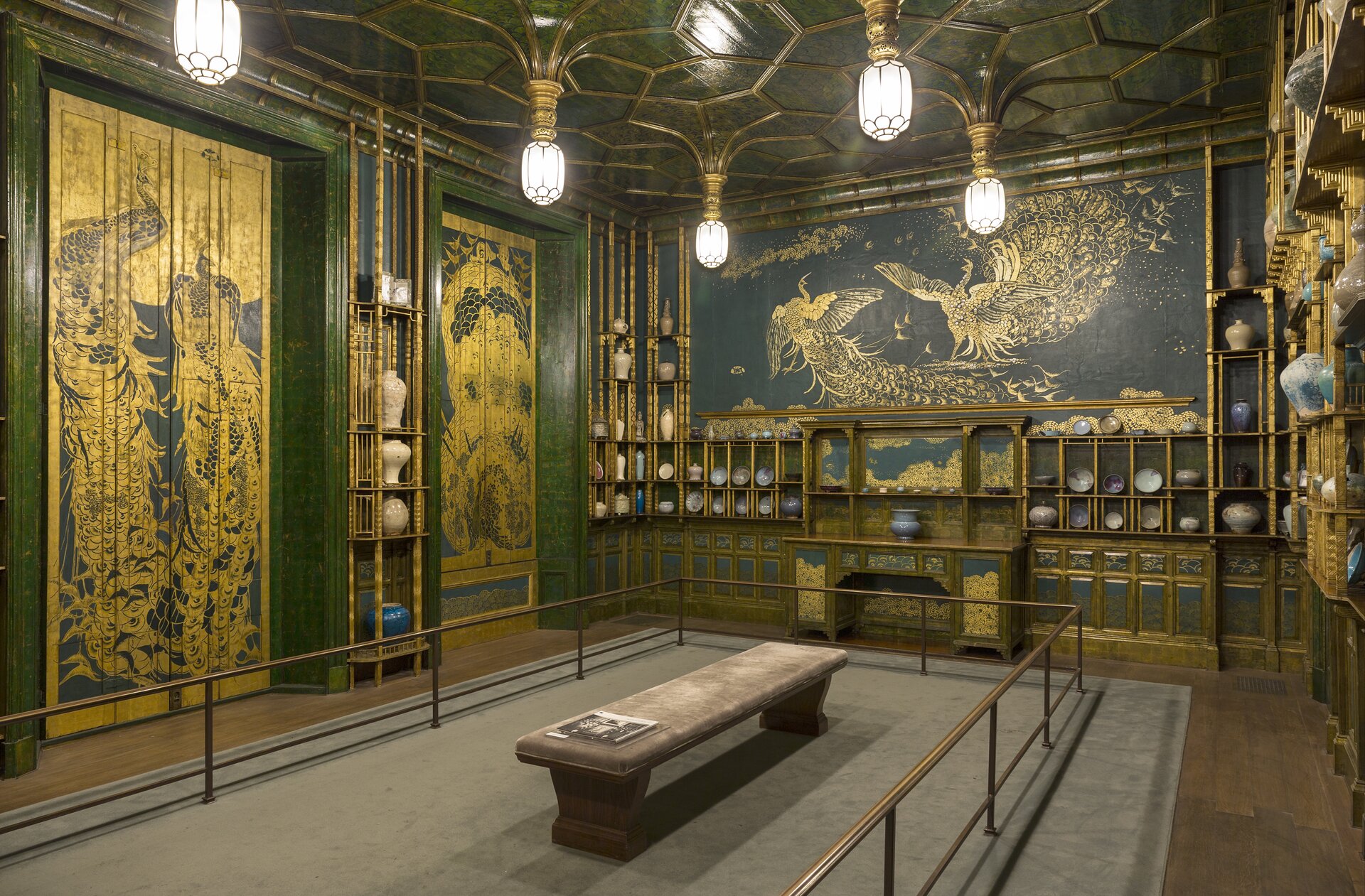 Ilustracja przedstawia zdjęcie pomieszczenia nazwanego „Pawia sala”, która jest pracą Jamesa Whistlera. Pomieszczenie jest obszerne i posiada bogato zdobione ściany ornamentami na bocznych ścianach oraz dużym wizerunkiem pawia widocznym na ścianie głównej. Malunek ścienny przedstawia dwa pawie brodzące po wodzie. Pawie są koloru biało-złotego i są przedstawione na czarnej ścianie. Pod malowidłem widoczny jest kominek oraz meblościanka, na której ustawione są talerze, oraz wazy.