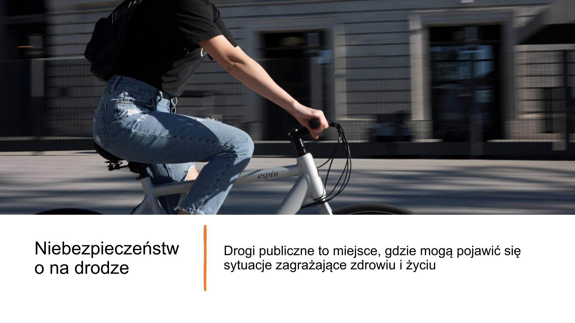 Niebieski slajd, na którym znajduje się tekst i zdjęcie. Ukazuje ono drogę, a obok chodnik i trasę rowerową. Przy chodniku rosną drzewa, które mają żółte liście. Po trasie rowerowej jedzie mężczyzna ubrany cały na czarno. Nad zdjęciem tekst: „Niebezpieczeństwo na drodze. Drogi publiczne to miejsce, gdzie mogą pojawić się sytuacje zagrażające zdrowiu i życiu”.