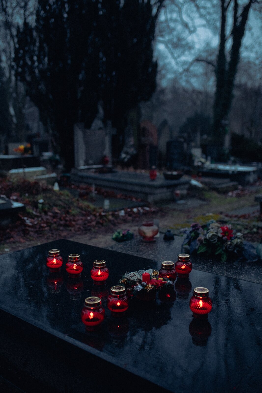 Zdjęcie przedstawia kamienną czarną płytę nagrobkową o wypolerowanej powierzchni, na której ułożone są znicze.