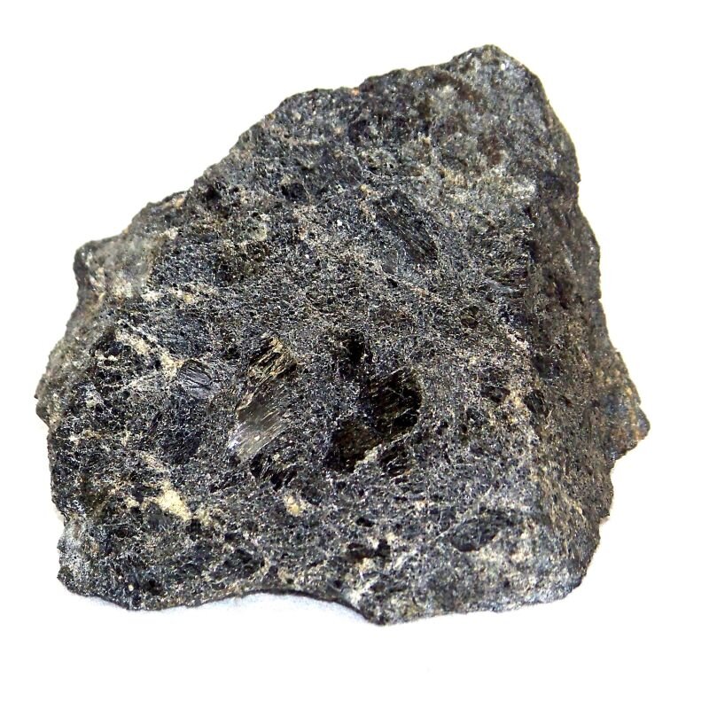 Na zdjęciu znajduje się ciemnoszary minerał o bezładnej, włóknistej teksturze. Miejscami ma porowatą powierzchnię. 
