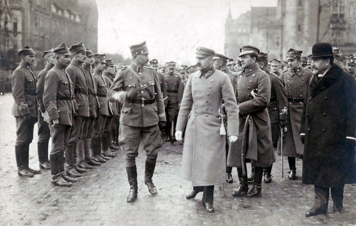 Zdjęcie przedstawia stojący na baczność oddział żołnierzy polskich. Przed oddziałem przechodzi grupa oficerów. Wśród nich jest Marszałek Józef Piłsudski.