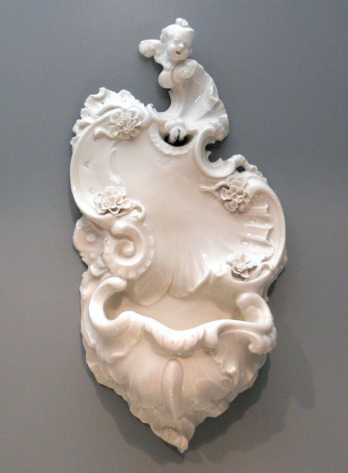 Ilustracjaprzedstawia Rocaille, czyli ornamenty asymetryczne. Ornament po lewej stronie jest wielokolorowy, przebiera kształt muszki. Ornament z lewej strony jest biały. 