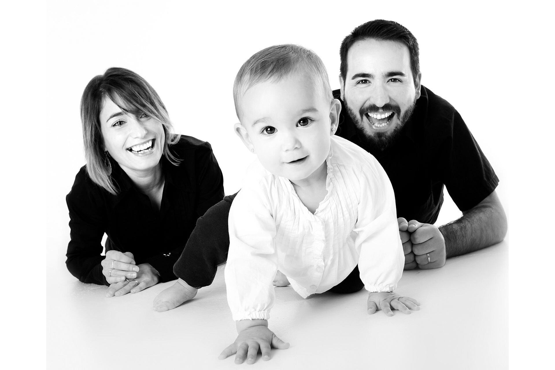 Zdjęcie przedstawia młodego mężczyznę i kobietę, którzy uśmiechają się, patrząc na raczkujące niemowlę.