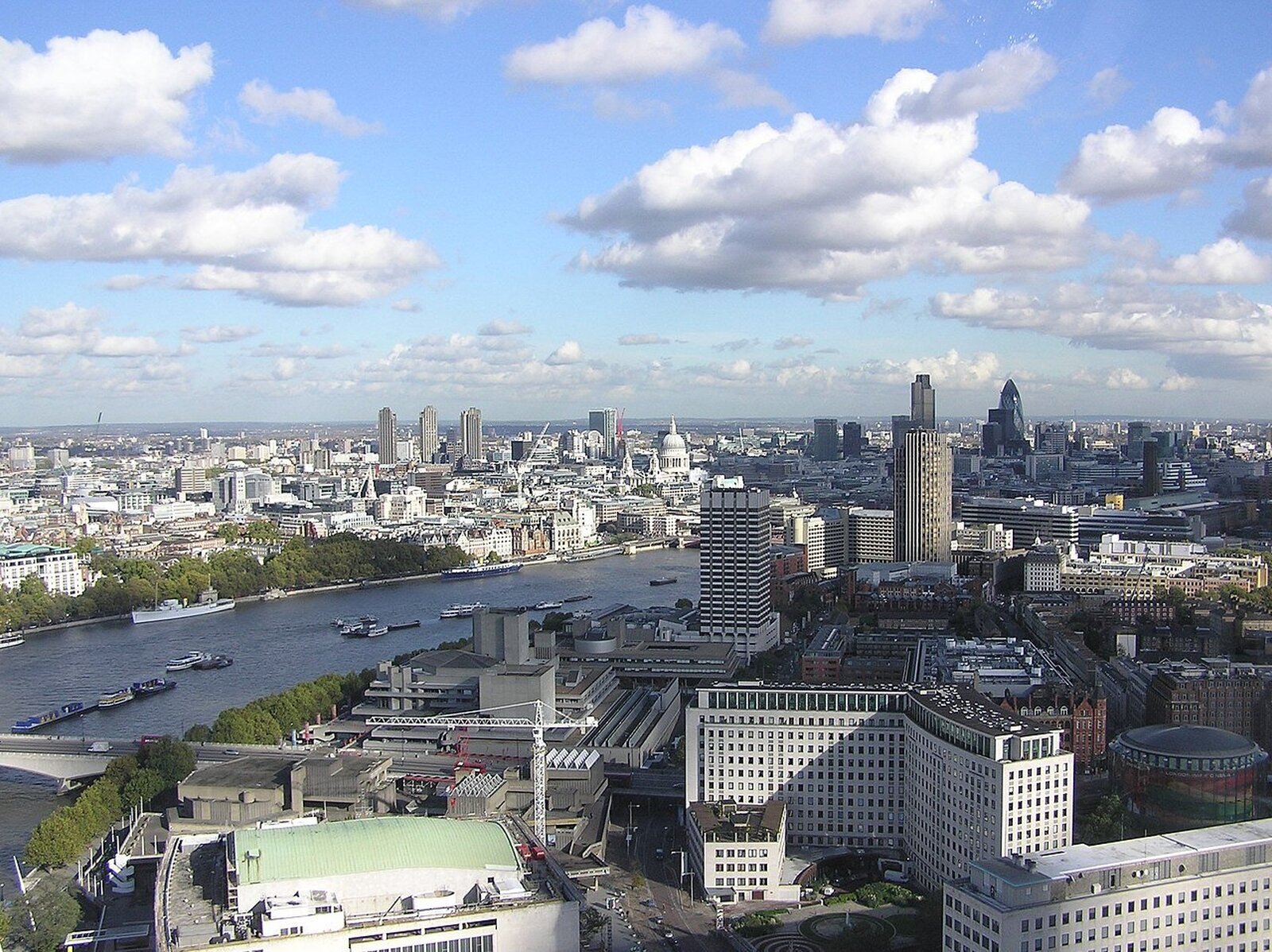 Fotografia lotnicza panoramy Londynu. Przez środek płynie rzeka, po bokach bardzo gęsta miejska zabudowa złożona z kamienic i wieżowców.