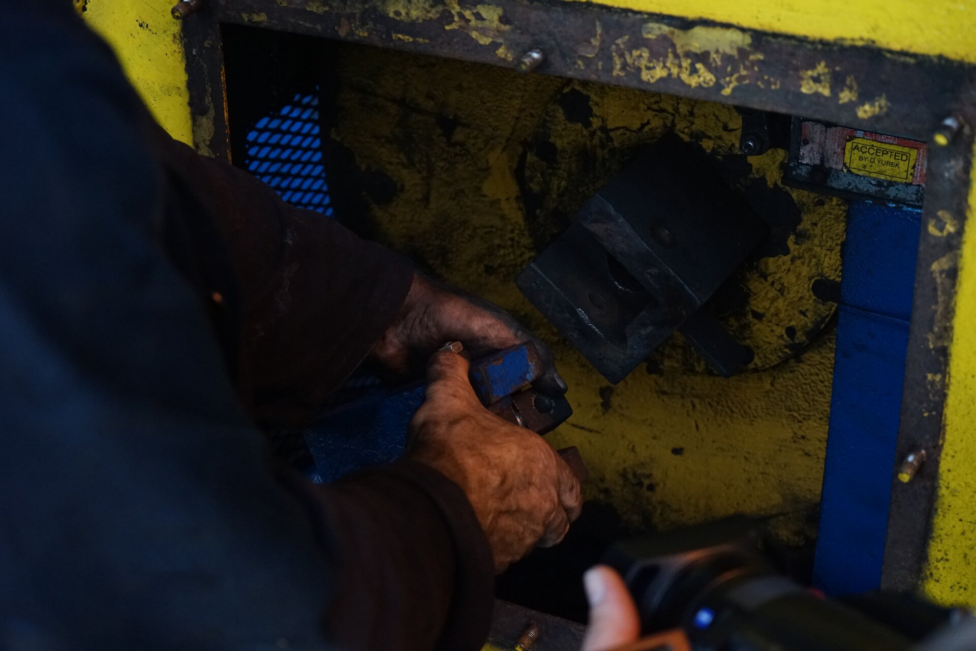 Zdjęcie przedstawia wirówkę podczas naprawy elementu zabezpieczającego w postaci kostki. Technik trzyma w dłoniach klucz, którym dokręca element zabezpieczający w postaci kostki. Kostka znajduje się na końcu osi obrotu wirówki. Odpowiada za zabezpieczenie urządzenia w przypadku przeciążenia lub zablokowania urządzenia w trakcie pracy. Poniżej zdjęcia znajduje się przycisk multimedialny z nagraniem audio. Treść nagrania jest zgodna z tytułem zdjęcia.